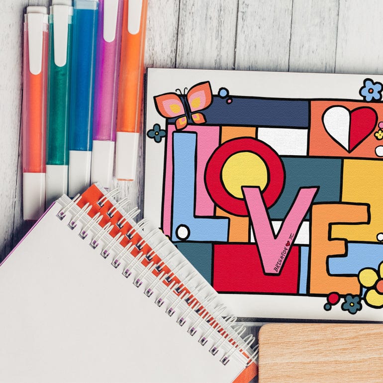 A flatlay shot of markers and a sketchbook showcasing the front artwork of the Power Of Love Tote