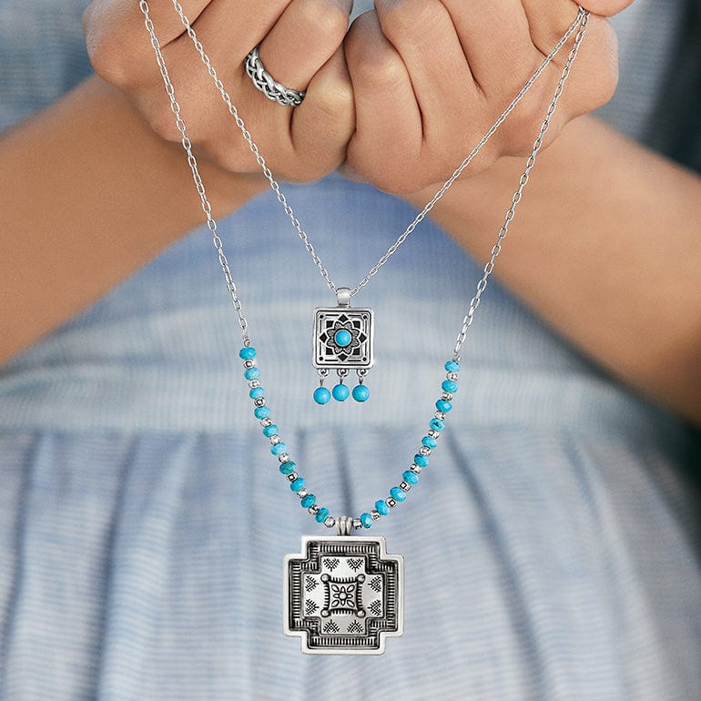 Close-up of model holding two silver and turquoise necklaces