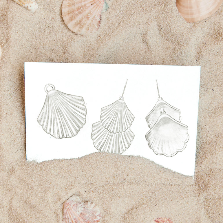 A sketch of shells on a piece of paper half buried in sand