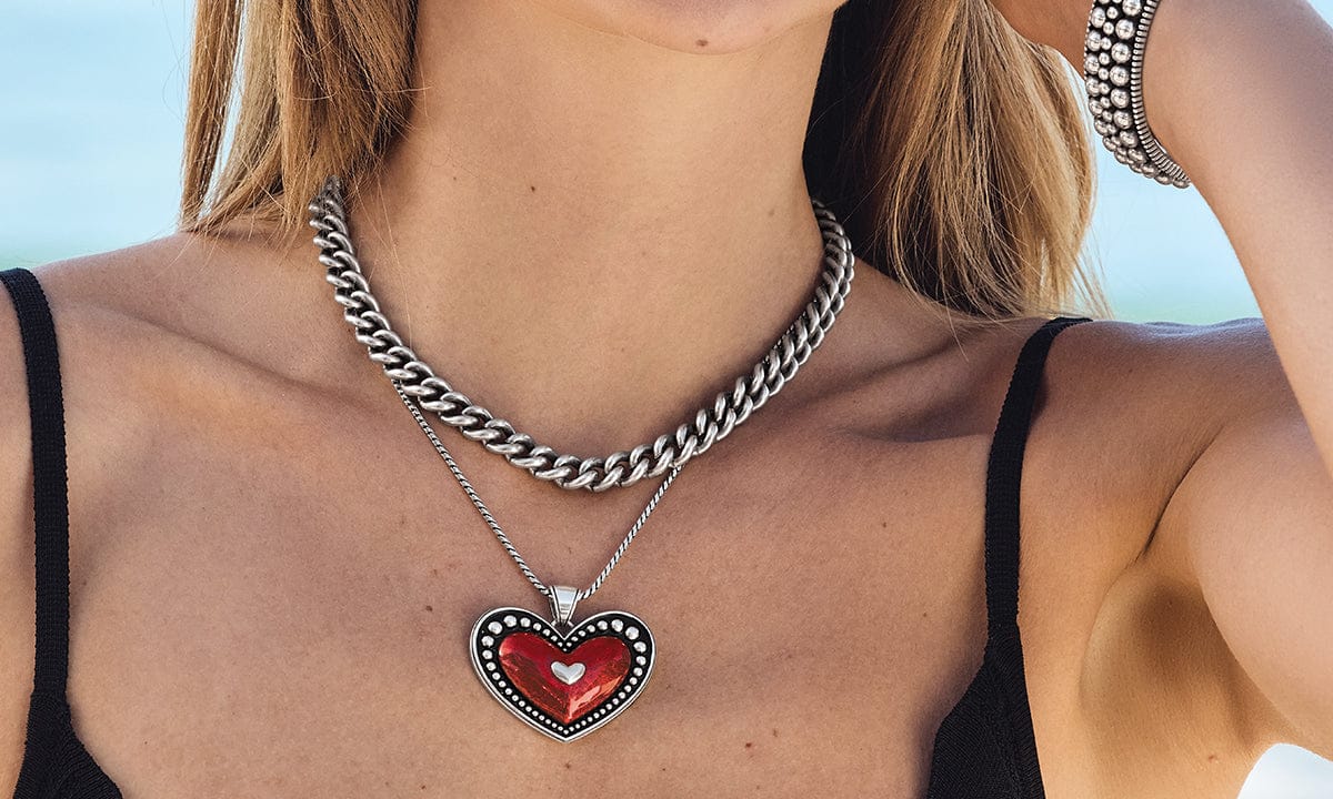 Person wearing a Brighton necklace with a red heart pendant against a blurred background