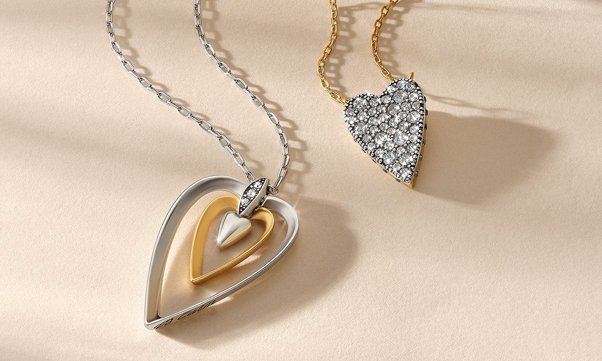 Two heart-shaped diamond Brighton pendants on gold chains against a beige background