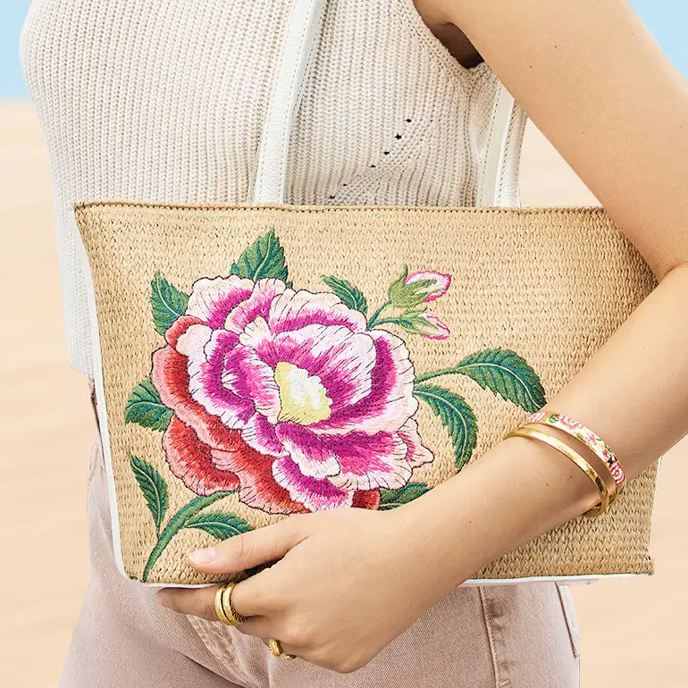 Person holding a Brighton straw clutch with floral embroidery against a light background