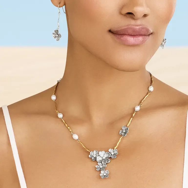 Woman wearing a Brighton gold necklace with floral pendants on a beige background