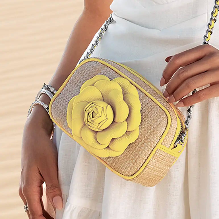 Brighton straw handbag with a yellow flower detail held by a person wearing a white dress.