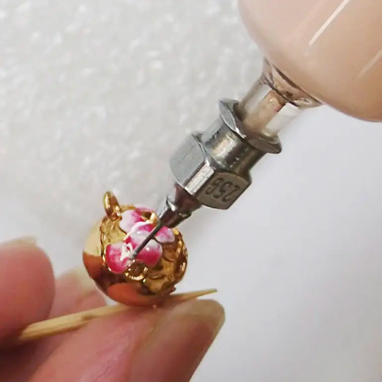 Close-up of a small gold and pink decorative item being worked on with a tool.