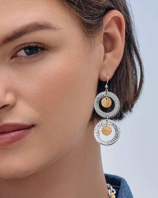 Close-up of a woman wearing Brighton silver and gold hoop earrings against a light background