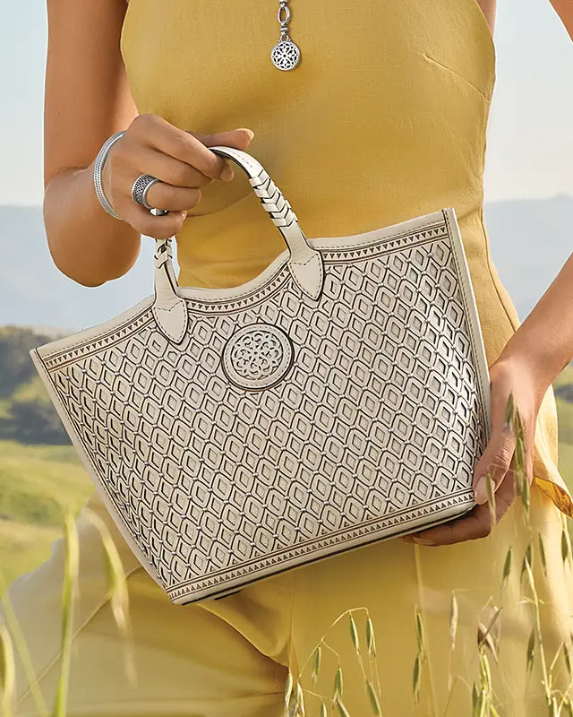 Person holding a patterned Brighton Leather handbag with a scenic background