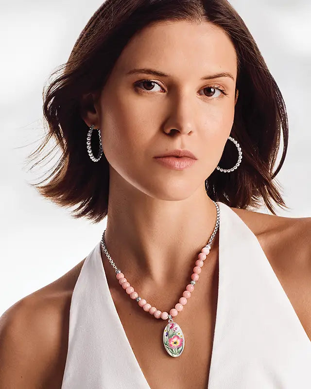 Woman wearing a Brighton necklace with a floral pendant on a plain background