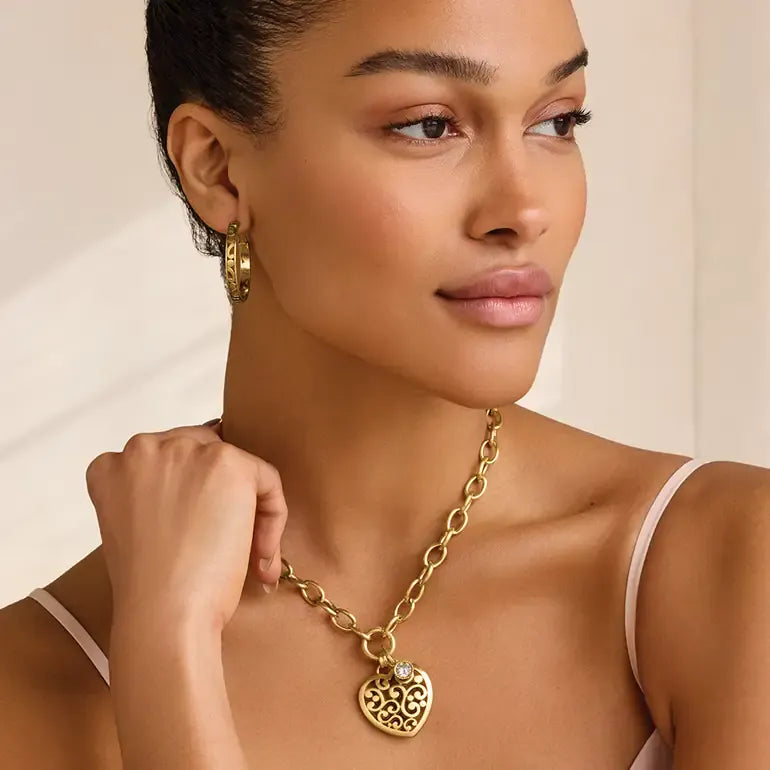 Woman wearing a gold necklace with a pendant against a neutral background