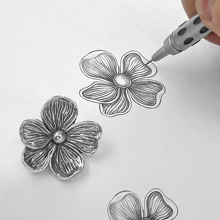 Silver floral designs on a white background with a hand holding a tool.