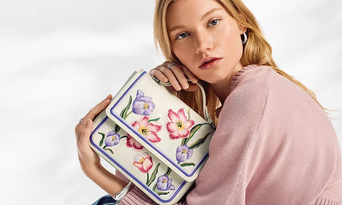 Woman holding a floral embroidered handbag against a white background