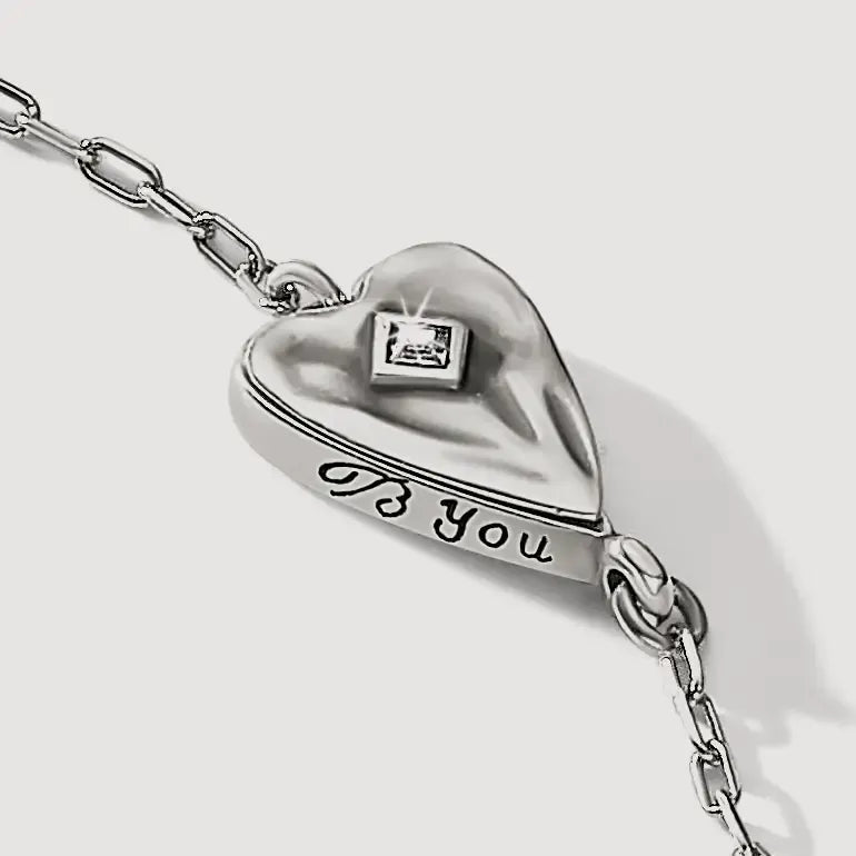 A silver heart-shaped pendant necklace engraved with 'B You' and featuring a small square gemstone, shown on a light gray background.
