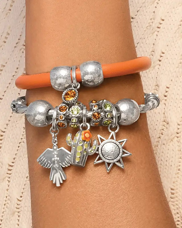 A close-up of a person's wrist wearing two bracelets. The top bracelet is orange with textured silver beads.