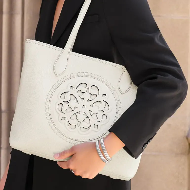 A person in a black blazer carries a large white pebbled leather tote bag with a circular cutout design on the front and matching shoulder straps.