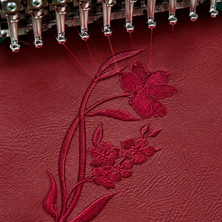 Close-up of a red leather surface with a floral embroidery design in matching red thread, with metallic embroidery needles visible at the top.