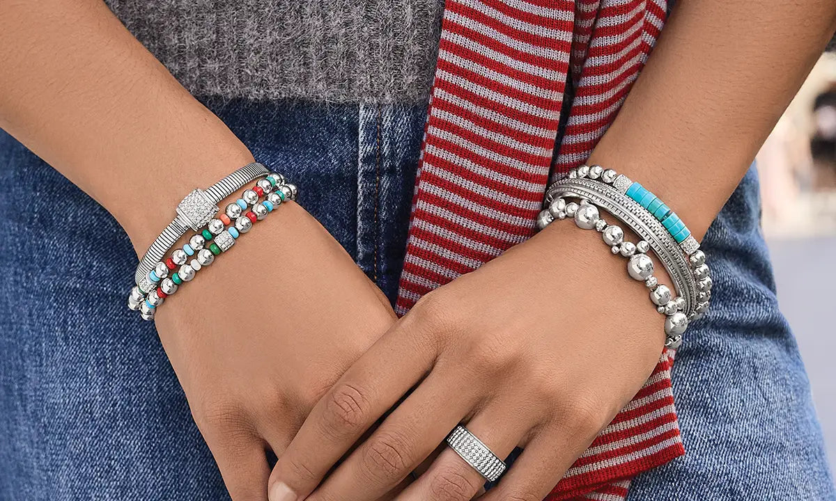 A woman's wrists wearing multiple bracelets. They are silver with colorful beads.