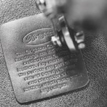 A close-up black and white photo of a leathercraft stamping tool pressing into a metal nameplate on textured leather, with the brand name 'Ripley' visible in the stamped logo.