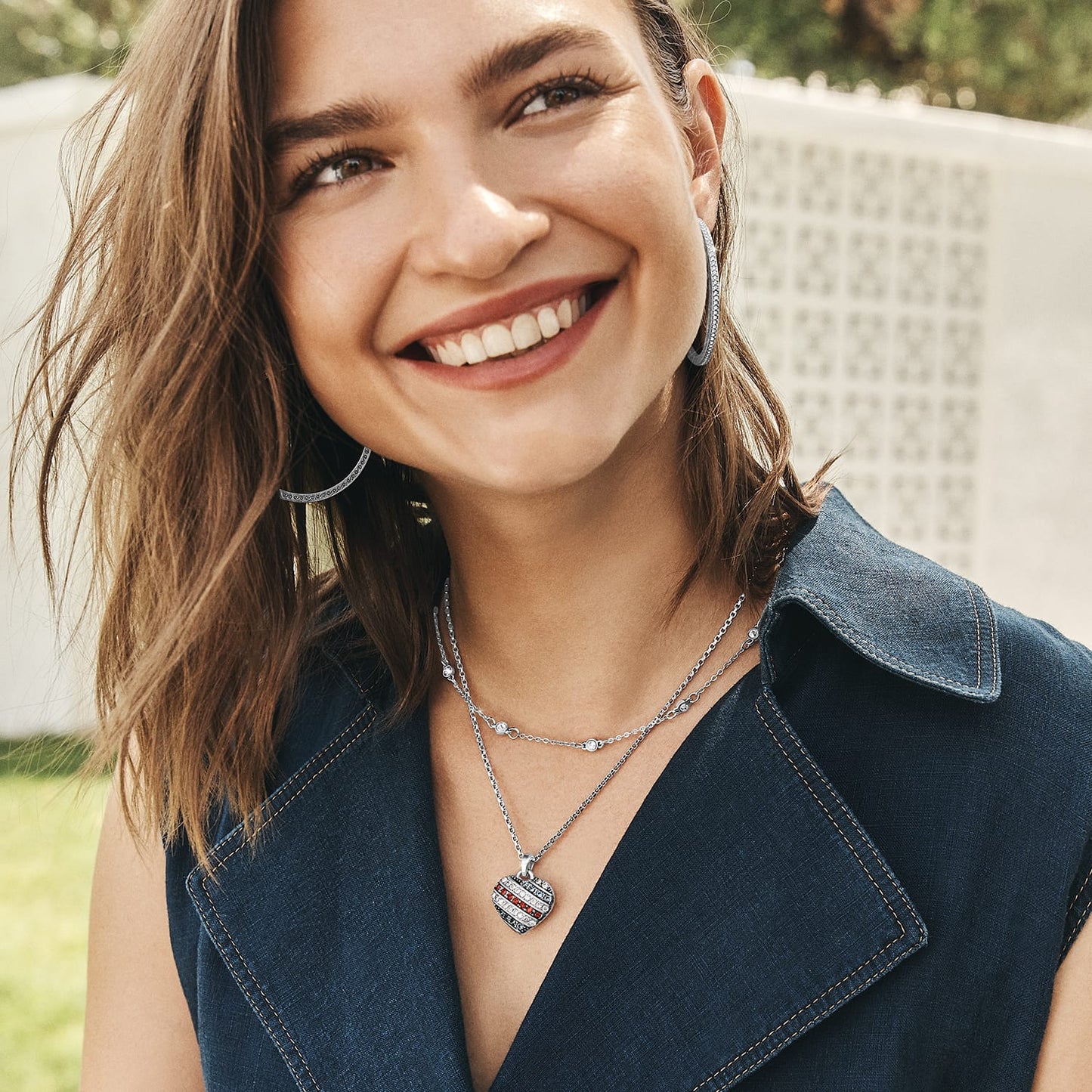 Model wearing Brighton silver-plated hoop earrings and layered necklaces with crystal accents and heart pendant