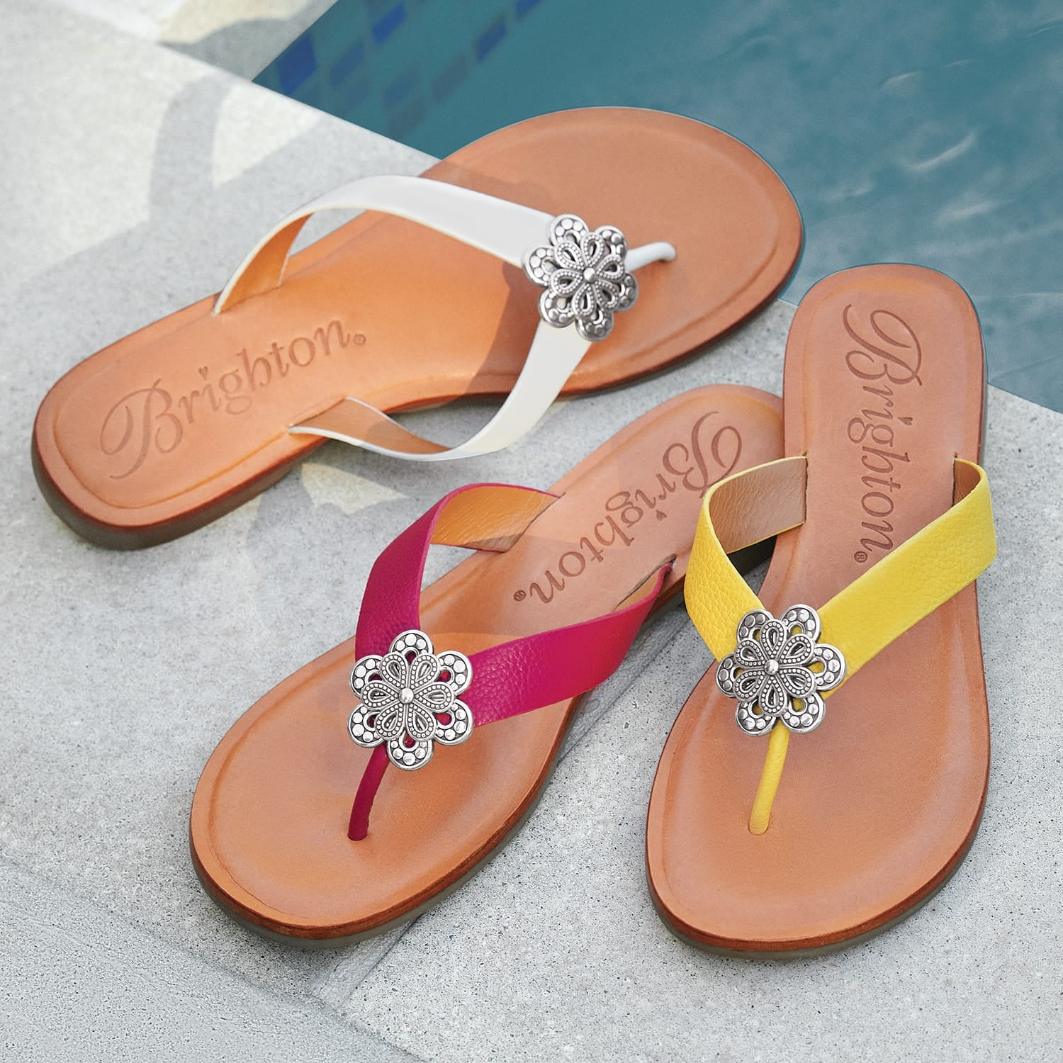 Brighton thong sandals in white, pink, and yellow with silver-tone floral medallions, styled poolside on stone tile