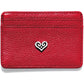 Brighton red pebbled leather card case with silver-tone scrolled heart emblem at center on a white background