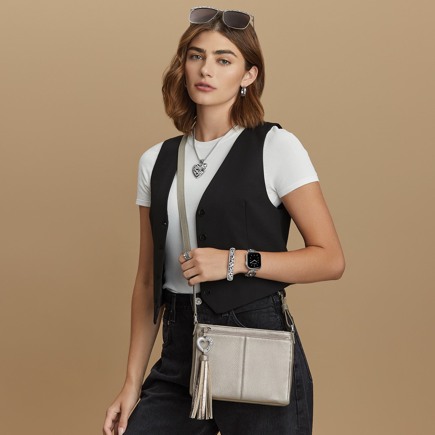 Model with a Brighton metallic leather crossbody handbag with tassel and silver heart charm, styled with coordinating Brighton accessories