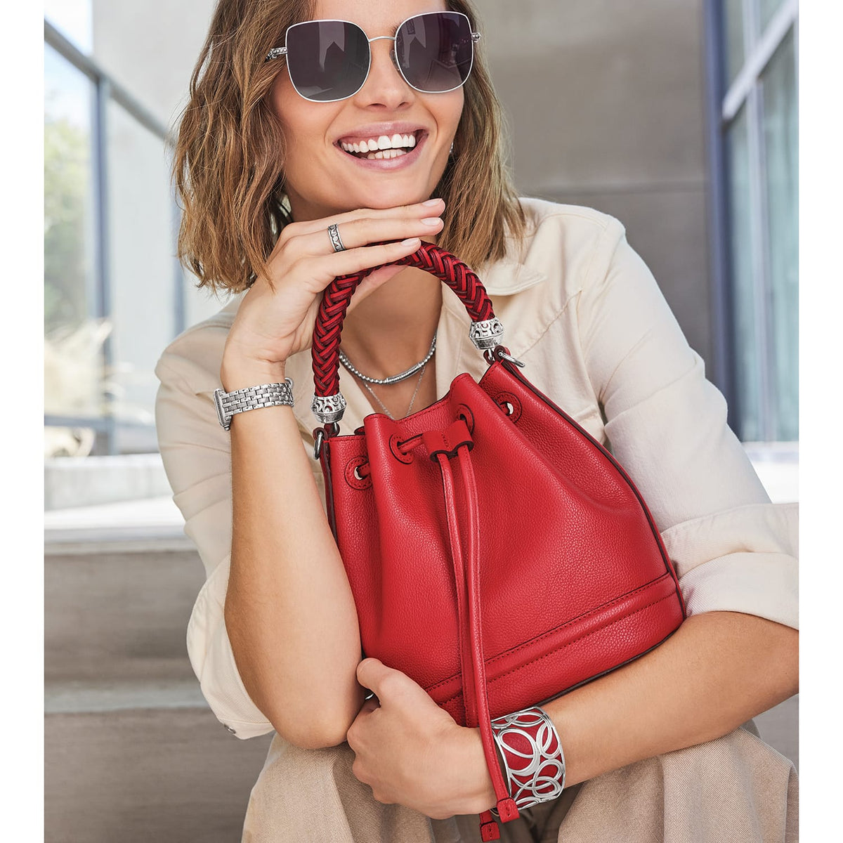Brighton red leather bucket handbag with braided top handle, styled with a silver cuff bracelet and sunglasses