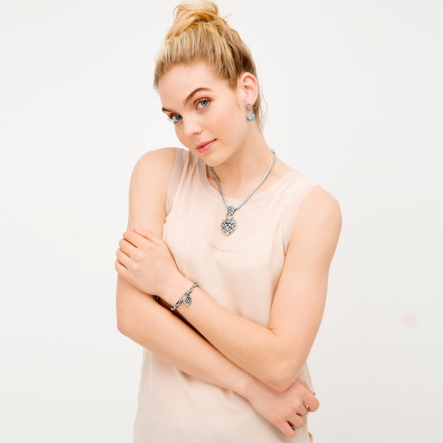 Model wearing a Brighton silver-plated heart pendant necklace with coordinating Brighton earrings and bracelet featuring filigree hearts