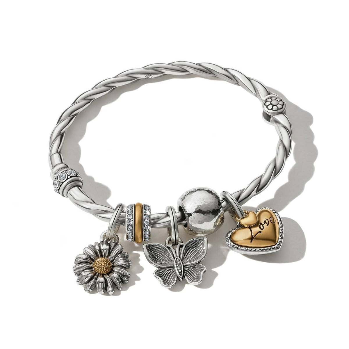 Brighton charm bangle bracelet with twisted silver-tone band, daisy, butterfly, and gold love heart charms on a white background