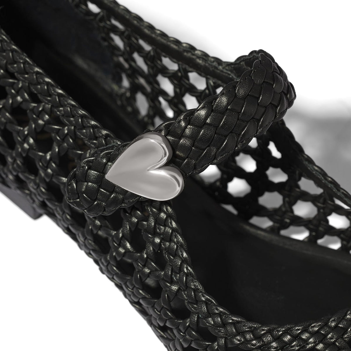 Close-up of Brighton woven black leather shoe with silver-tone heart accent on braided strap