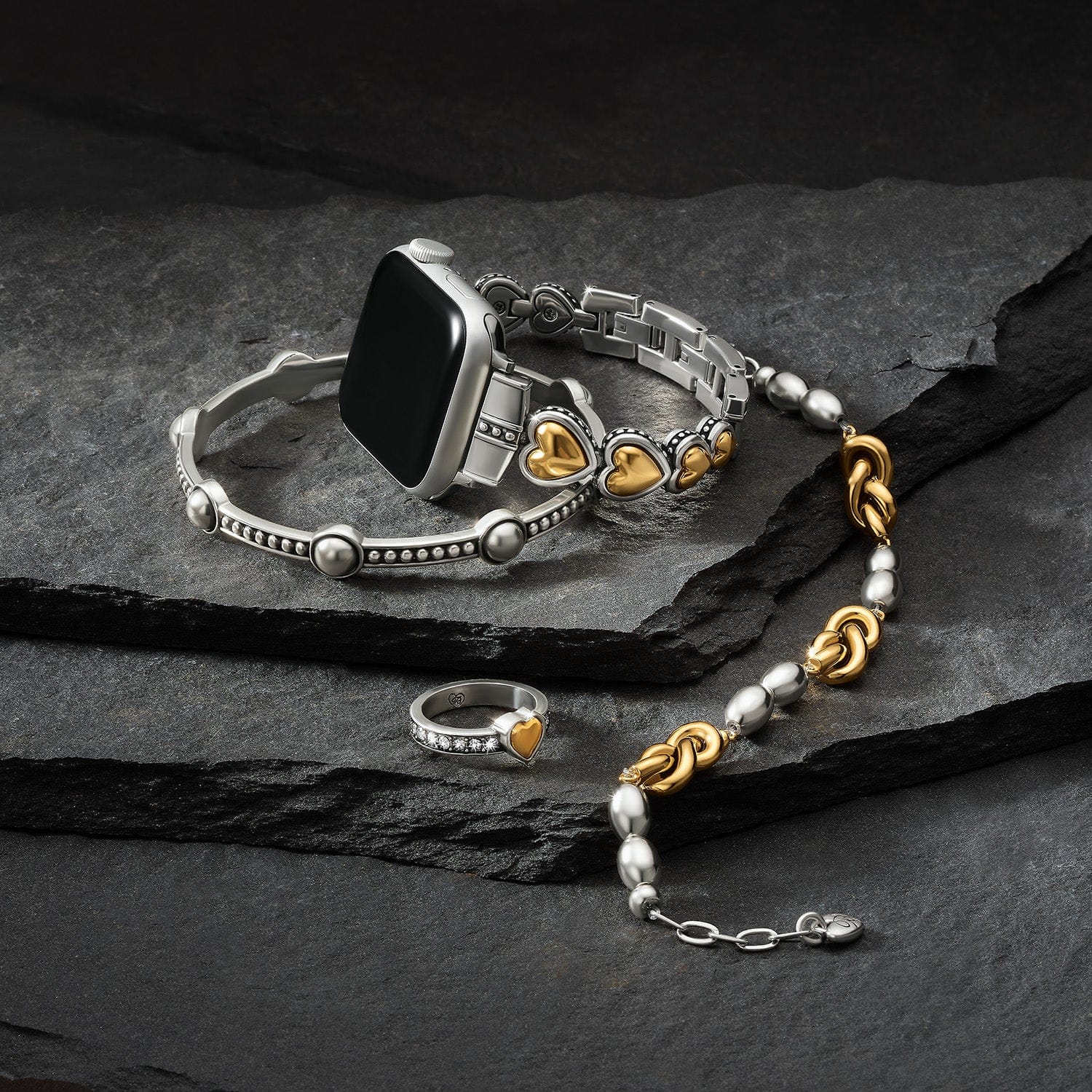 Silver and gold Brighton bracelet with heart charms on a dark stone surface