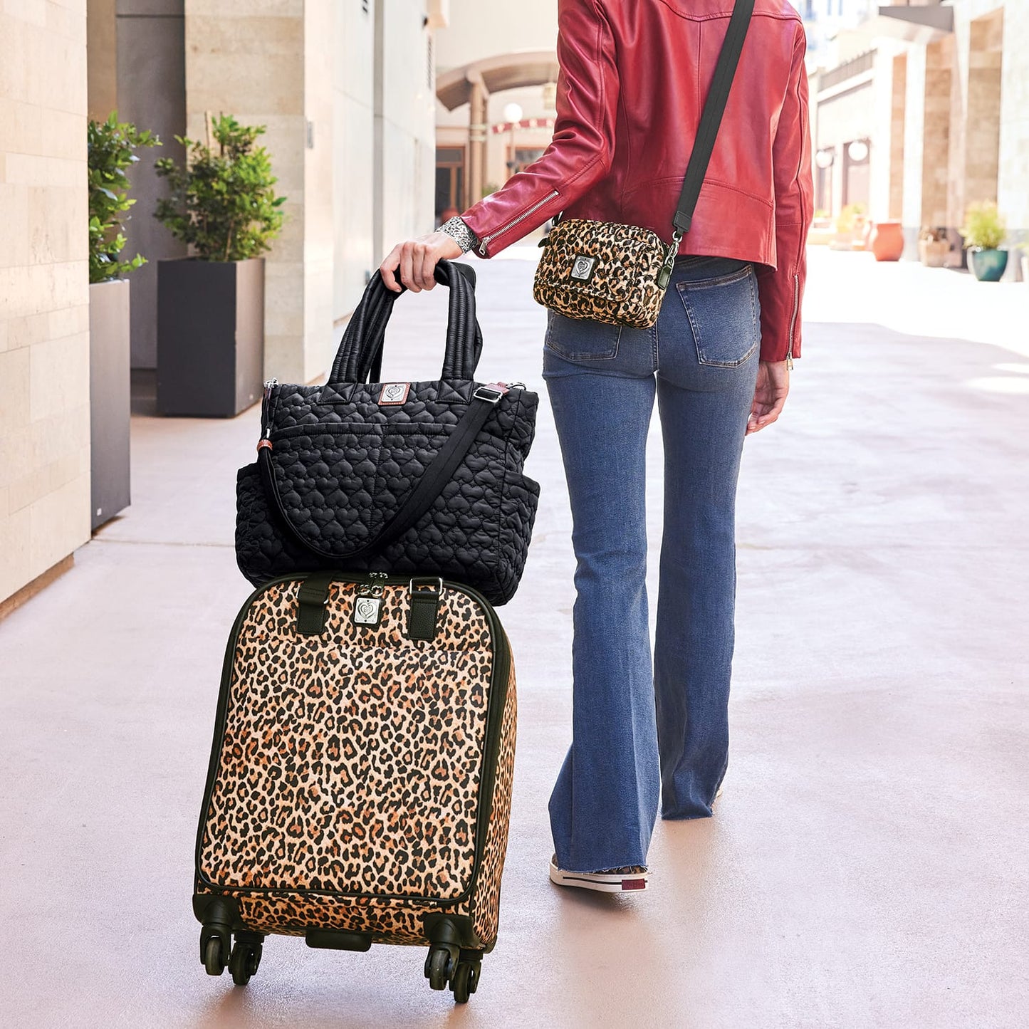 Model with a Brighton leopard print rolling suitcase, black quilted tote, and coordinating leopard crossbody bag