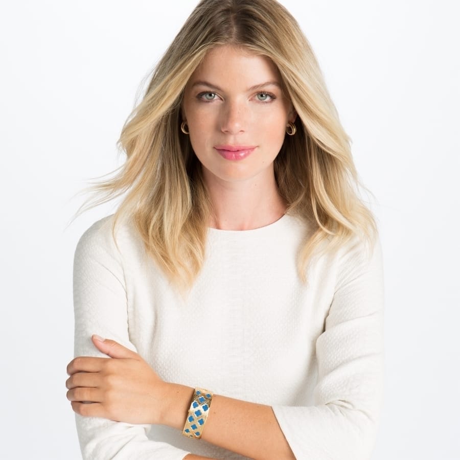 Model wearing a Brighton gold-plated hinged cuff bracelet with blue mosaic inlay paired with gold hoop earrings
