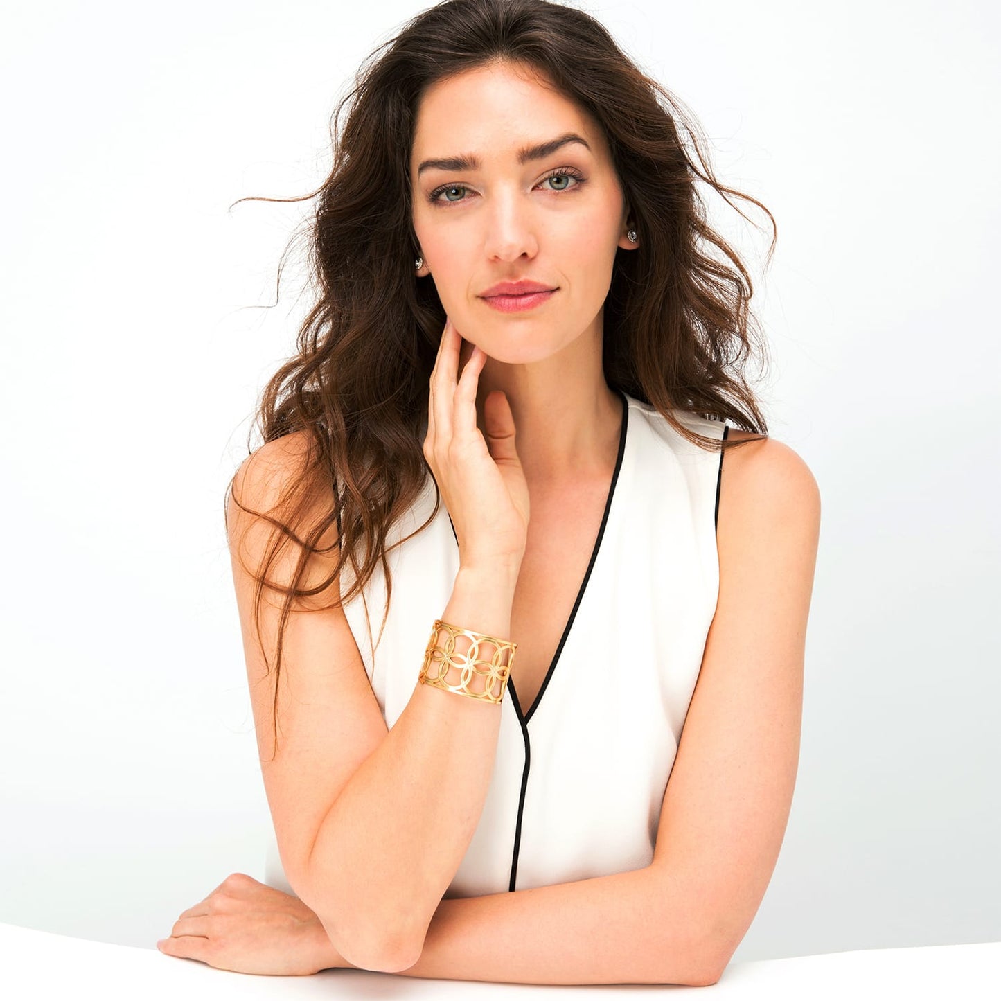 Model wearing a Brighton gold-plated cuff bracelet with openwork interlocking circle design, paired with crystal stud earrings