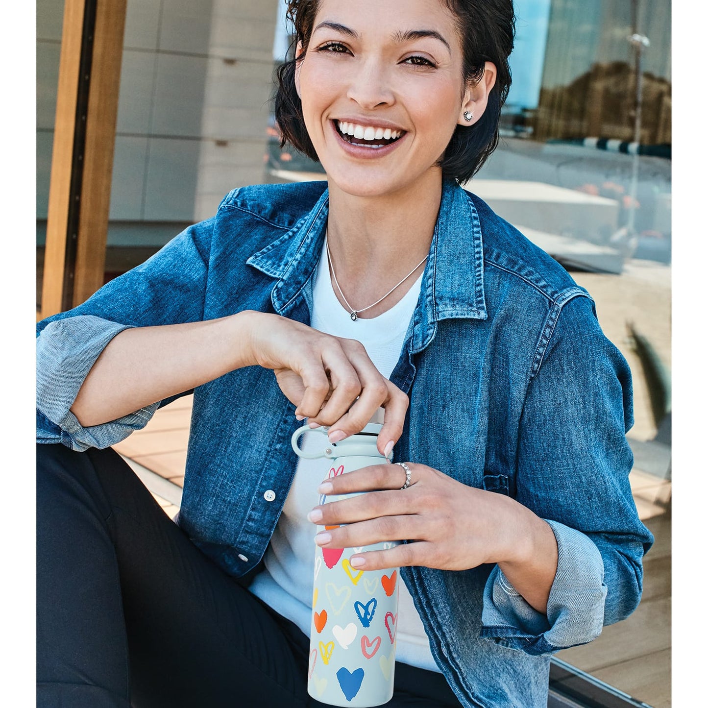 Model with a Brighton stainless steel water bottle featuring colorful heart print and light blue background