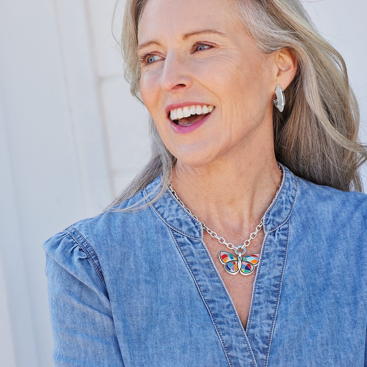 Model wearing a Brighton silver-plated butterfly pendant necklace with colorful enamel wings paired with silver-plated hoop earrings