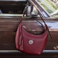 Brighton burgundy leather hobo handbag with silver-tone medallion and leather tassels, hanging on a vintage car door