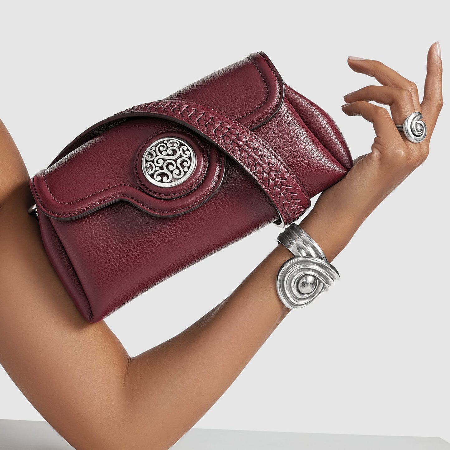 Brighton burgundy leather handbag with silver medallion accent and braided detail, styled with a silver cuff bracelet
