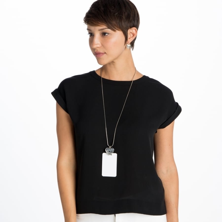 Model wearing a Brighton long silver-plated pendant necklace with heart pendant and rectangular tag charm