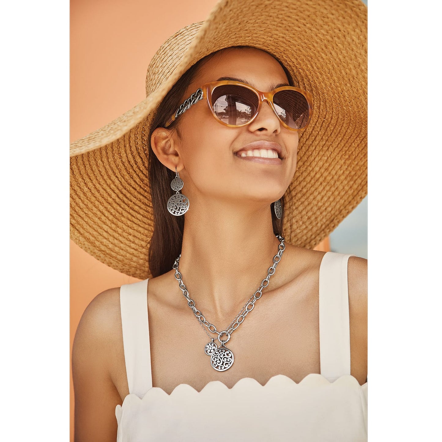Model wearing Brighton silver-plated drop earrings with ornate scroll medallions paired with a matching layered pendant necklace