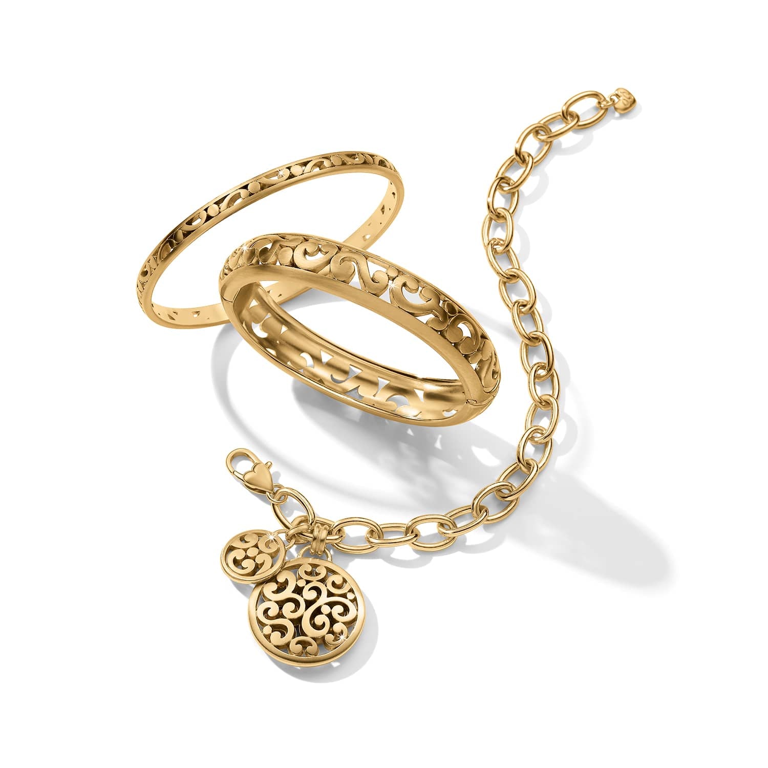 Brighton gold-plated bracelets styled with two scroll-pattern bangles and a chain bracelet with medallion charms on white
