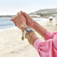 Model wearing a Brighton white braided watch band with coordinating Brighton accessories including gold-plated bangles and charm bracelet