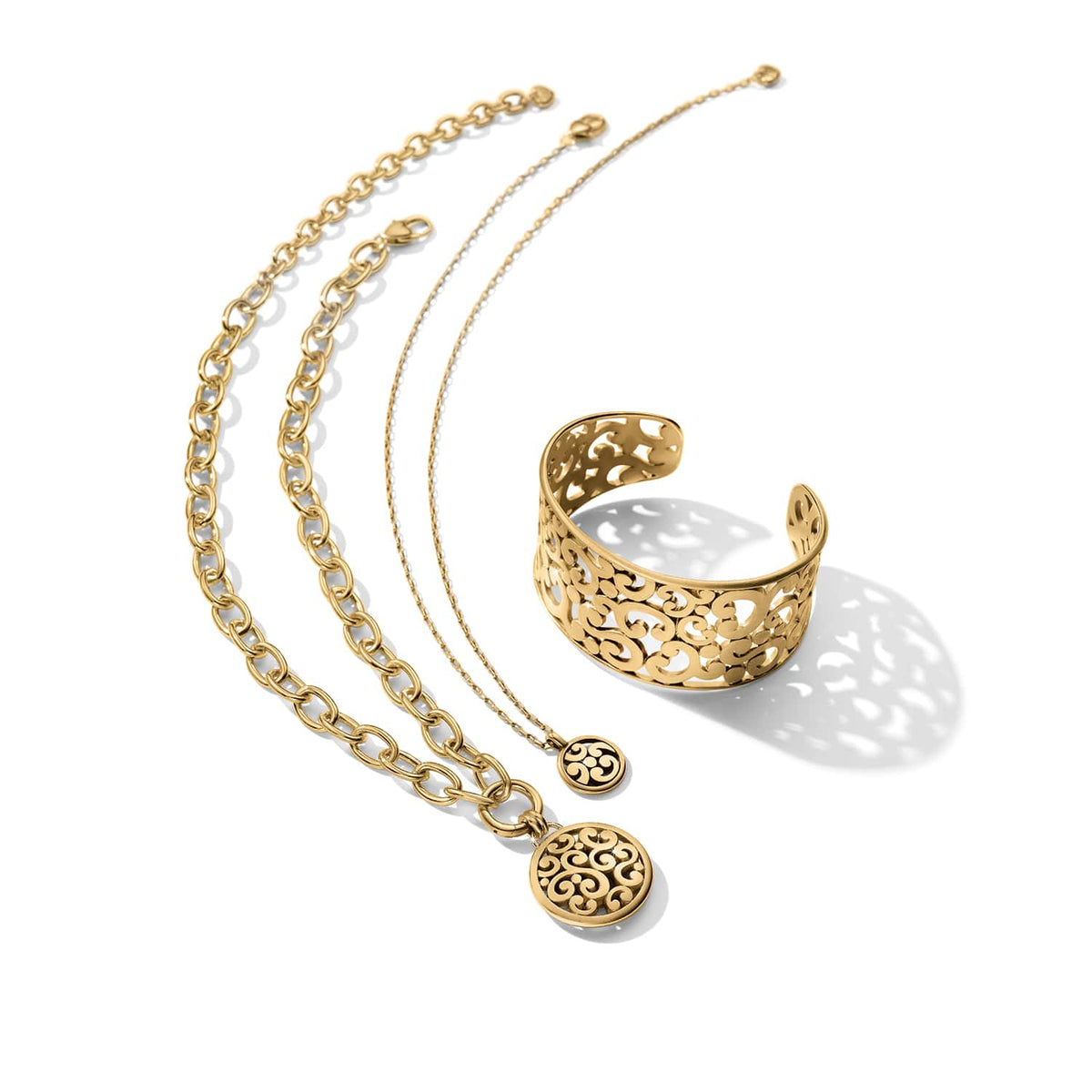 Brighton gold-plated jewelry set styled with a scroll-pattern cuff bracelet and matching pendant necklaces on white