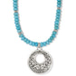 Brighton pendant necklace with dyed howlite turquoise beads and silver-plated openwork scroll medallion on a white background