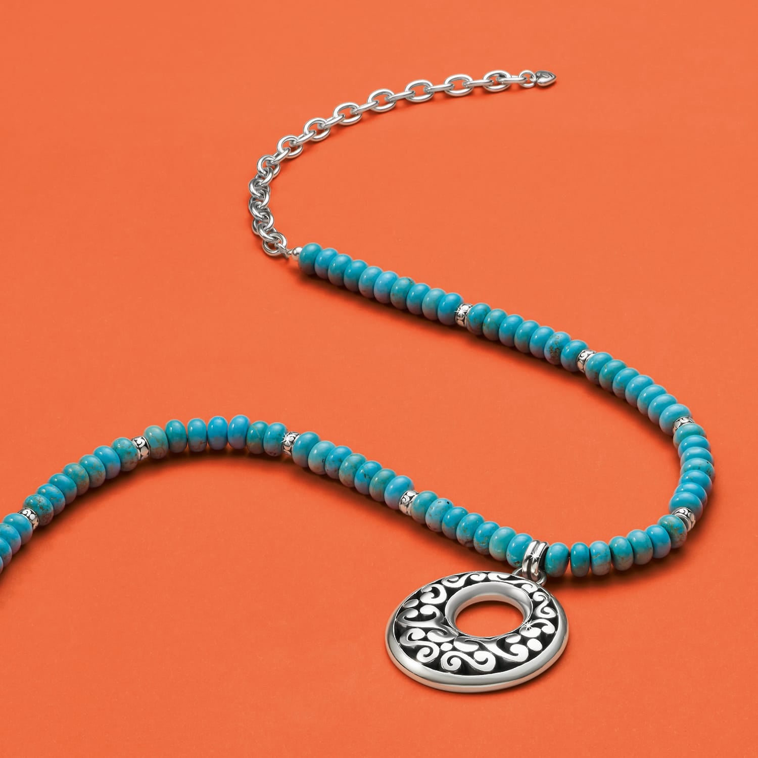 Brighton beaded necklace with dyed howlite beads, silver-plated chain, and open scroll pendant on an orange background