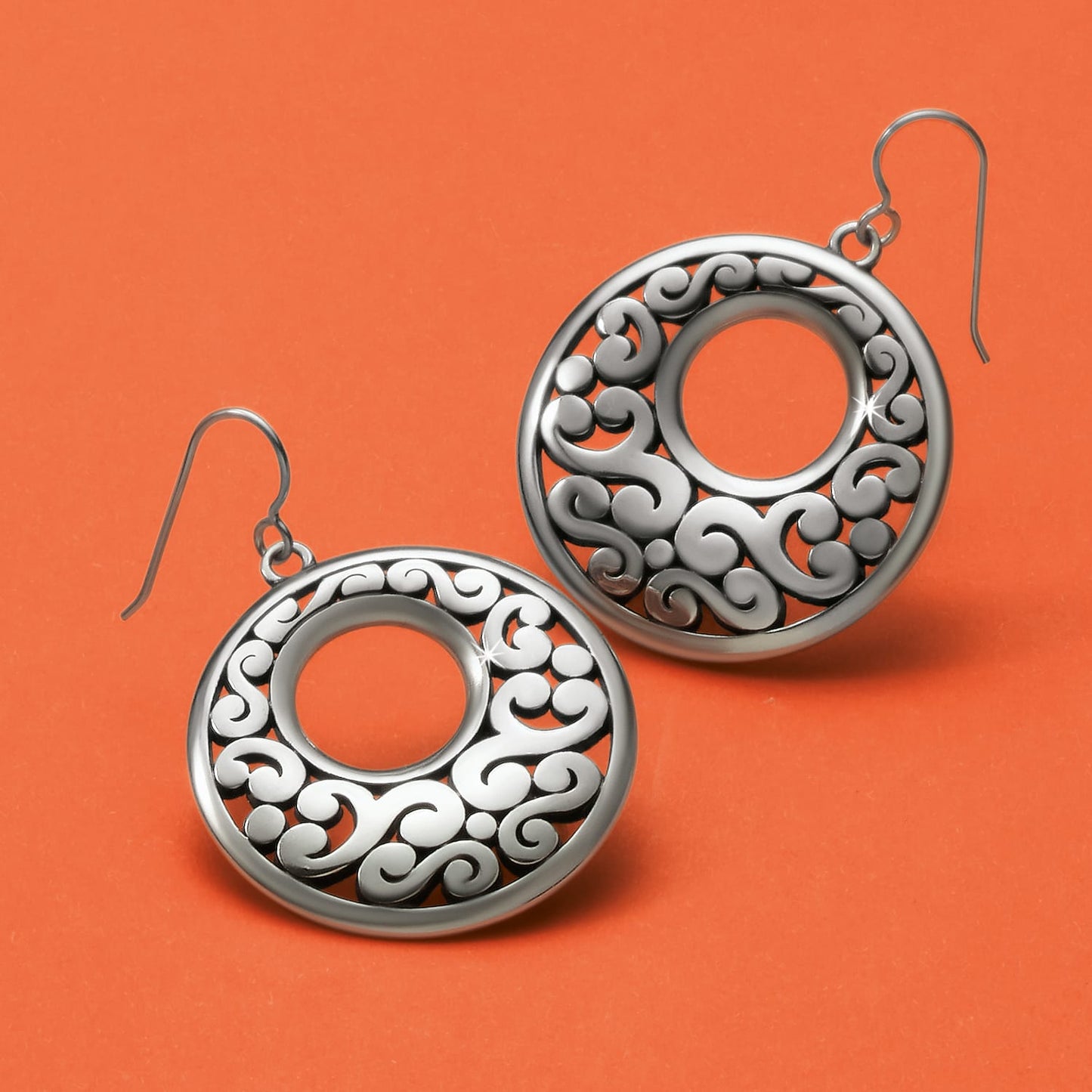 Brighton drop earrings with silver-plated open circle design and scroll detailing on an orange background