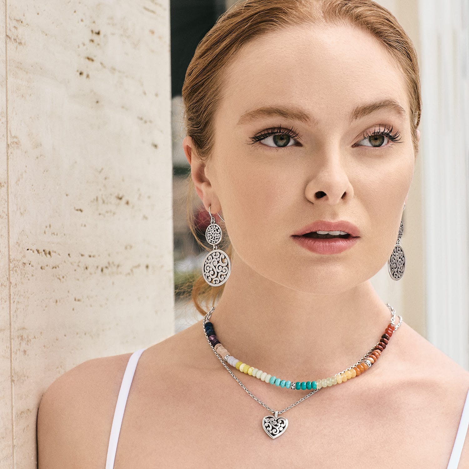 Model wearing Brighton silver-plated scroll drop earrings and layered beaded necklace with silver-plated heart pendant