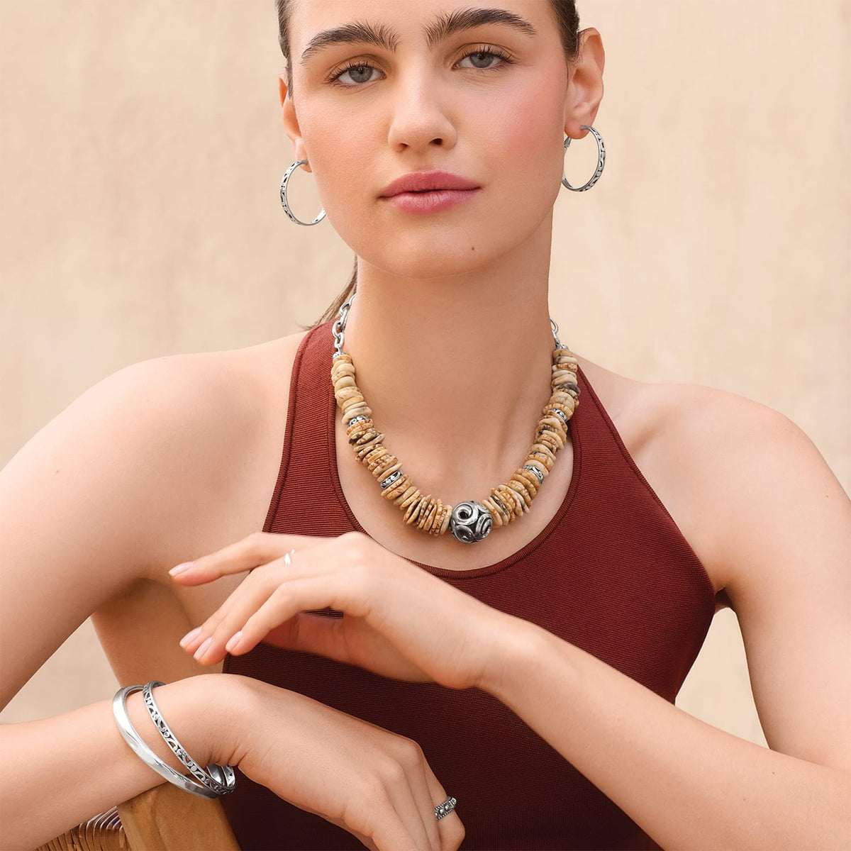 Model wearing a Brighton necklace with tan disk beads and silver-plated ornate centerpiece, with coordinating Brighton accessories