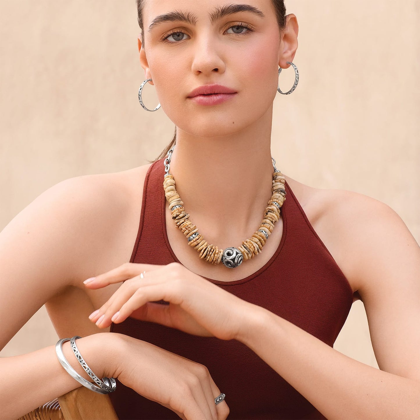 Model wearing a Brighton necklace with tan disk beads and silver-plated ornate centerpiece, with coordinating Brighton accessories