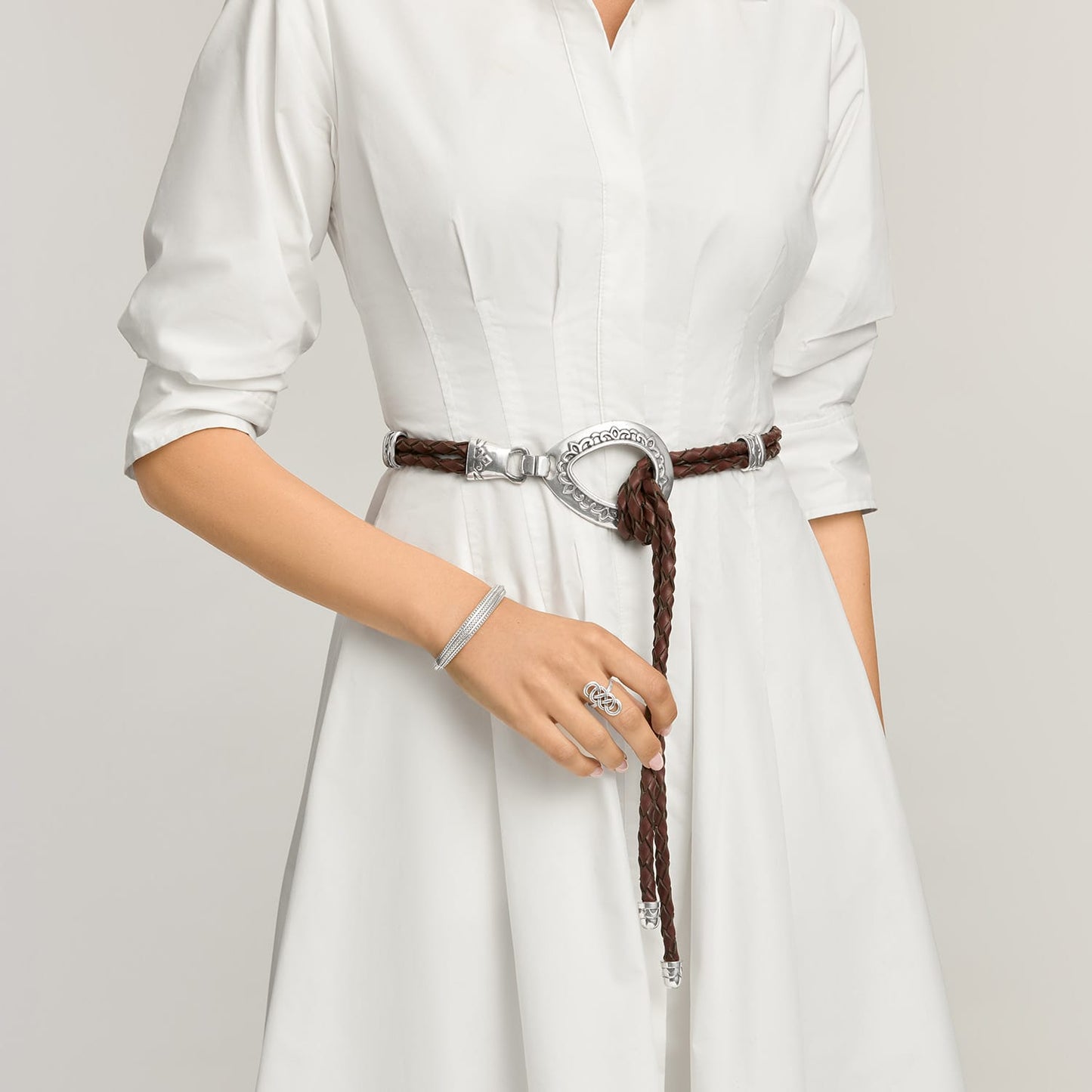 Model wearing a Brighton braided brown leather belt with ornate silver-tone oval buckle and hook closure