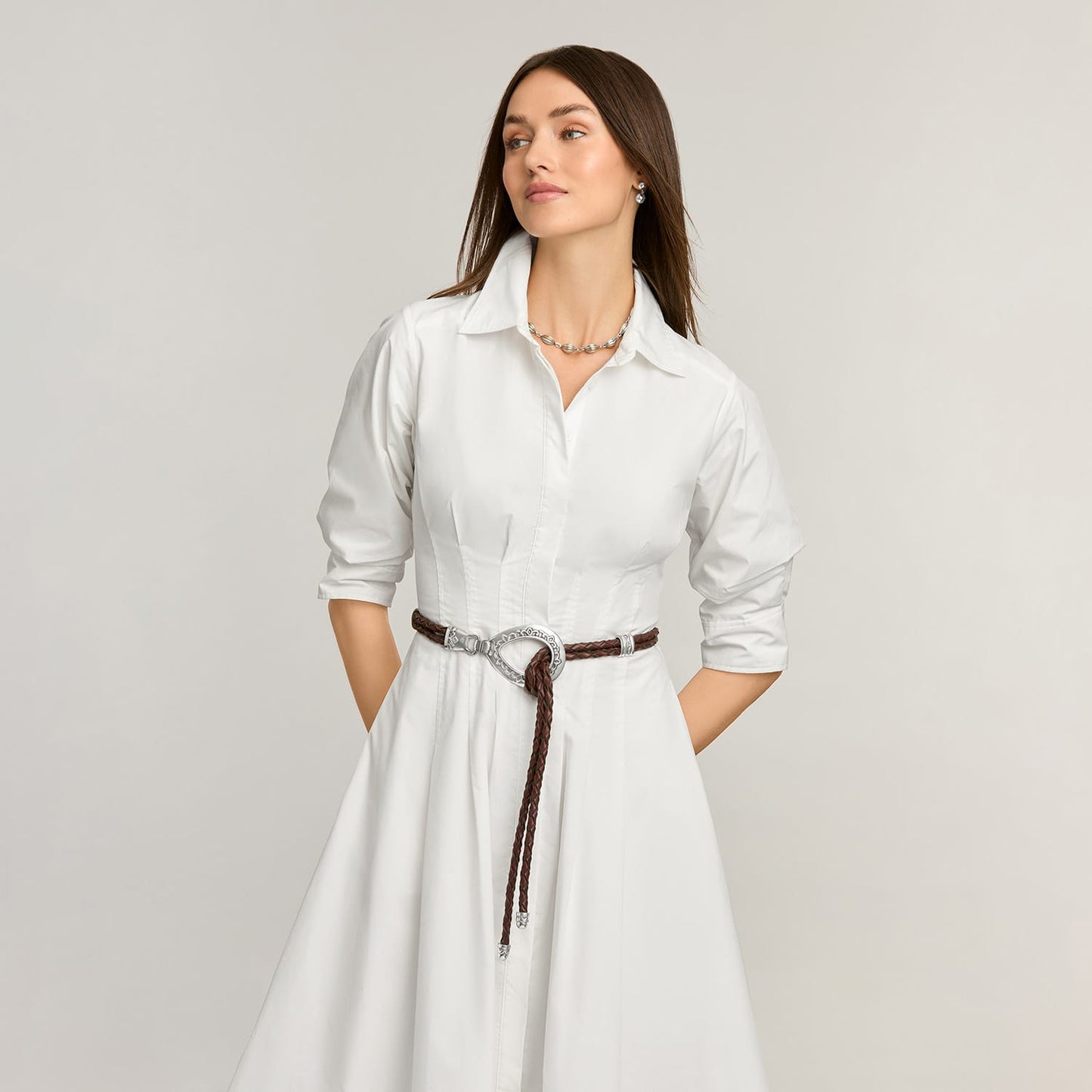 Model wearing a Brighton braided brown leather belt with silver-tone equestrian buckle over a white shirtdress